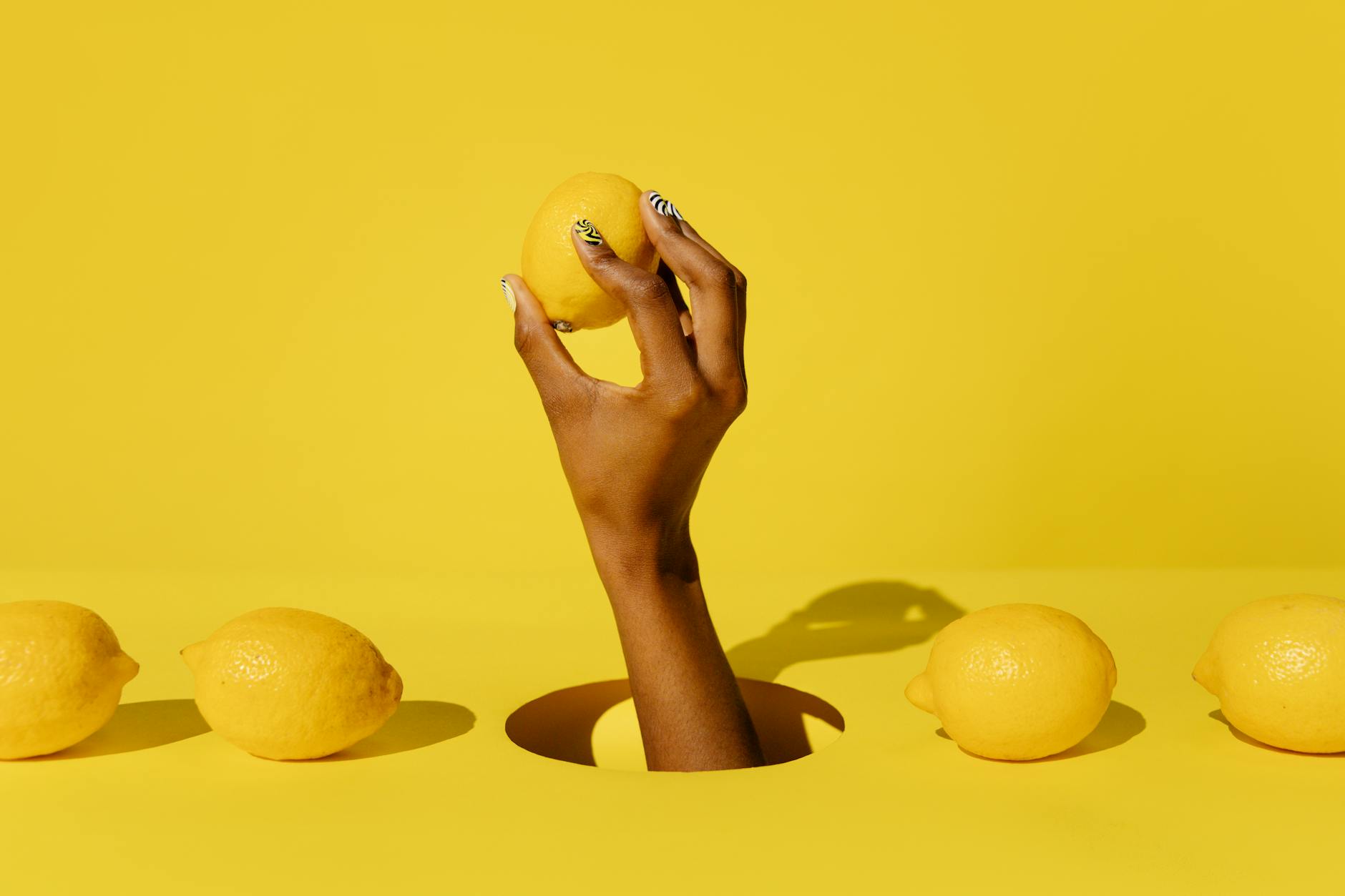 A hand holding a bright yellow lemon against a vivid yellow background, symbolizing fresh, intentional pleasure.