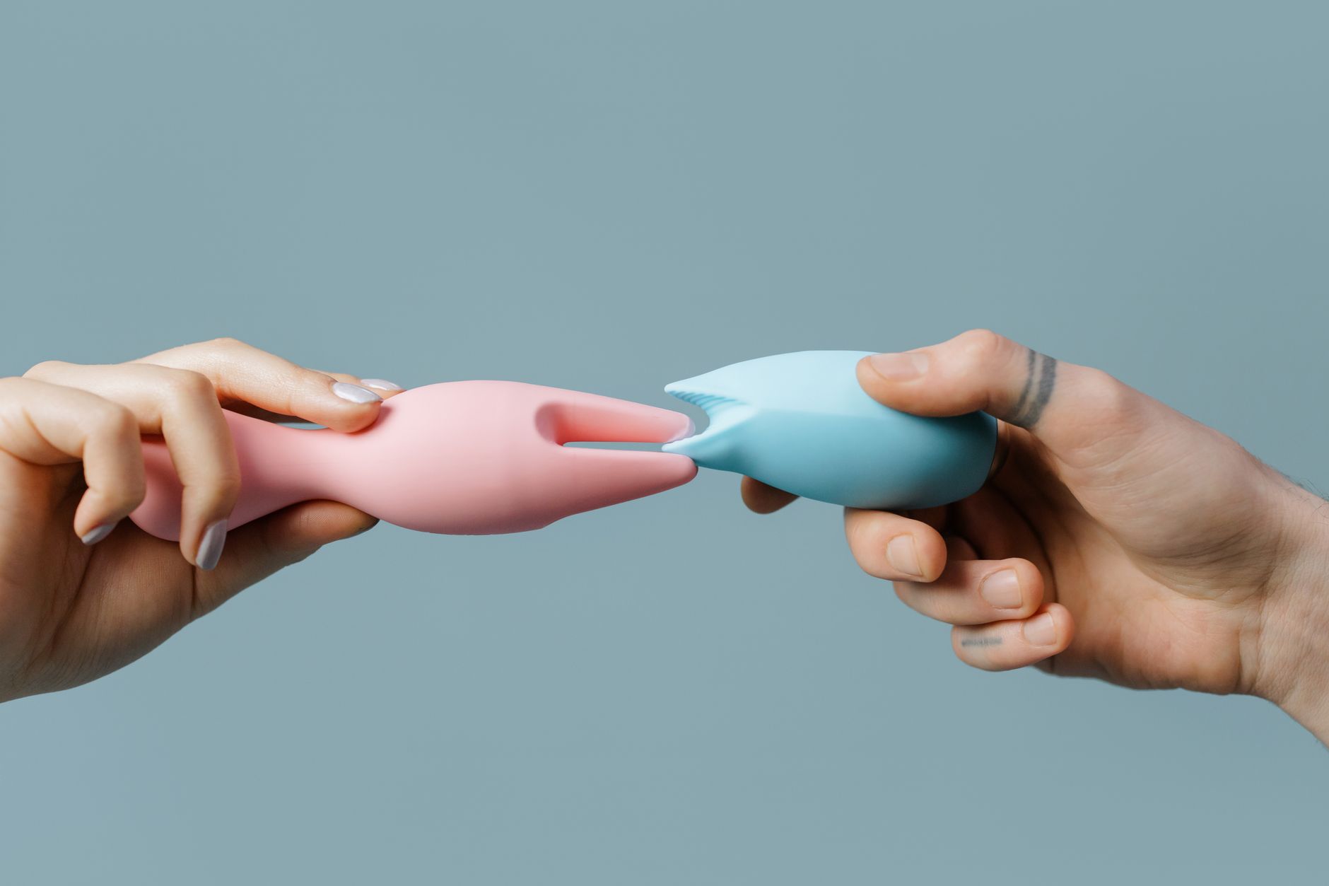 Two hands holding pastel-colored silicone sex toys, symbolizing shared pleasure between partners