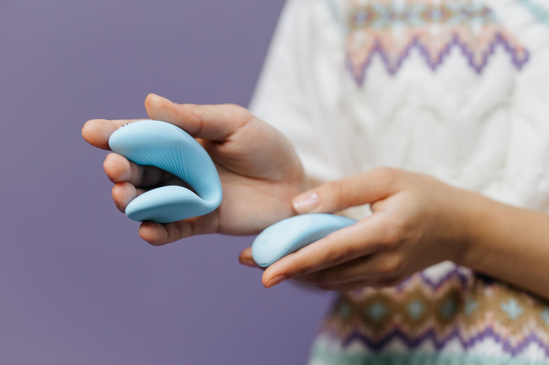 Close-up of hands holding a sleek blue vibrator against a purple background, representing modern intimacy tools