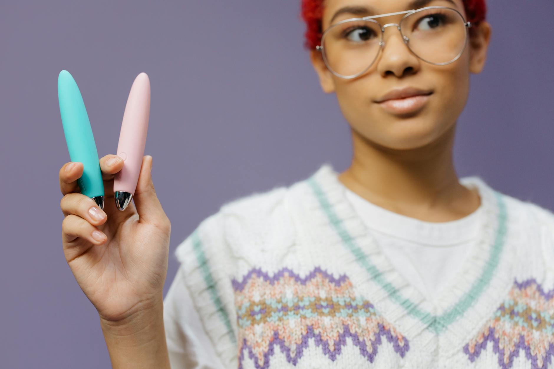 A woman holding colorful vibrators against a purple background, representing pleasure and choice