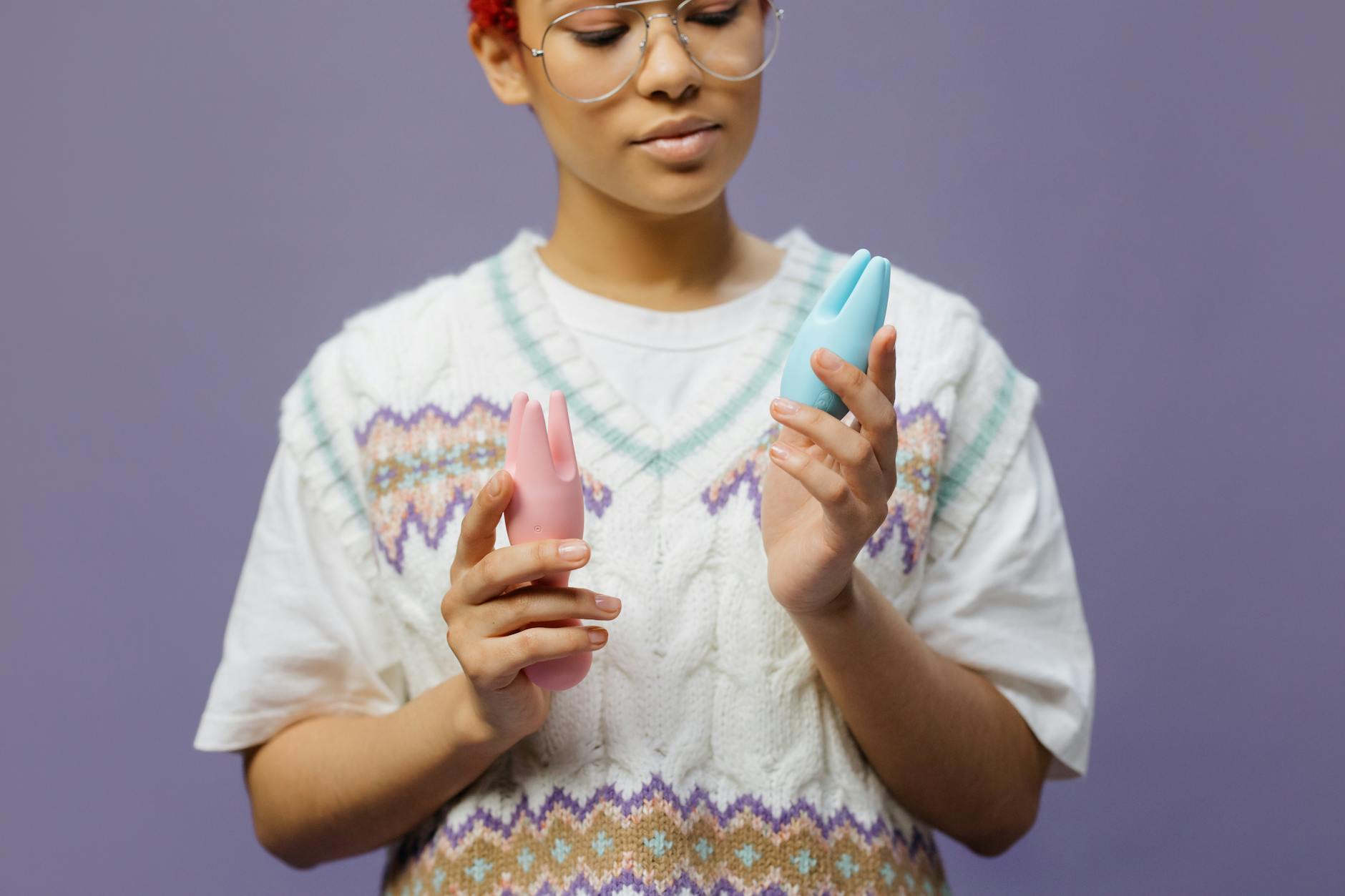 Woman holding blue and pink silicone vibrators in a contemplative manner, exploring pleasure during hormonal transition