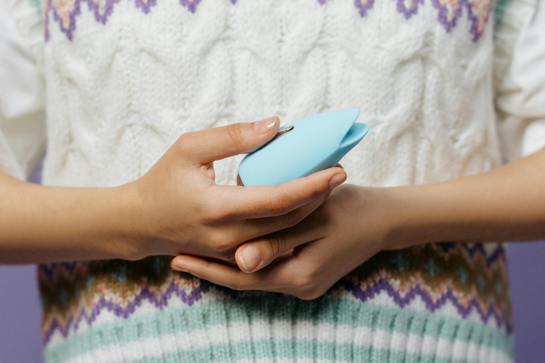 Woman holding a blue and pink silicone vibrator with a thoughtful expression while wearing eyeglasses.