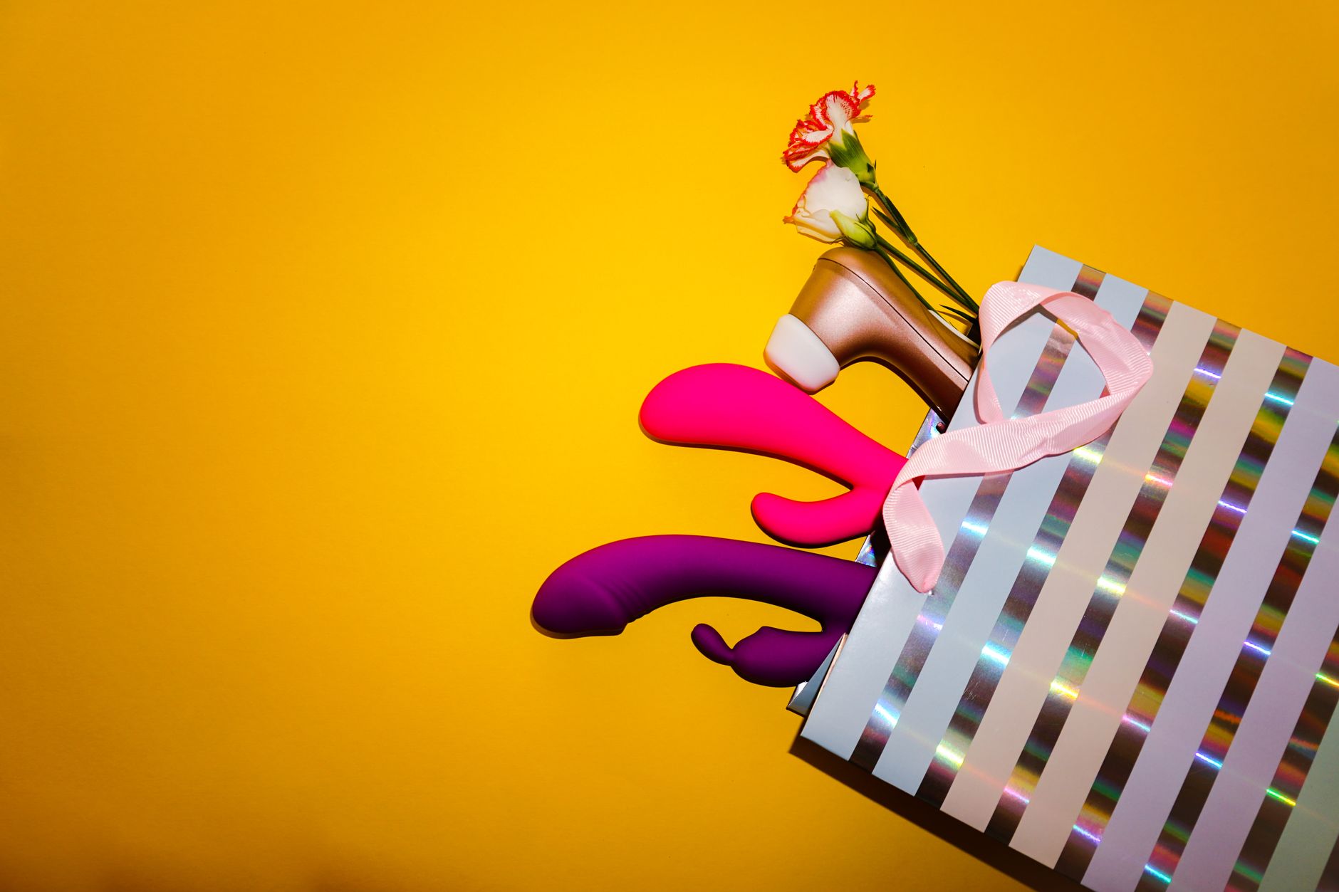 Colorful vibrators with flowers in a gift bag against a bright yellow background
